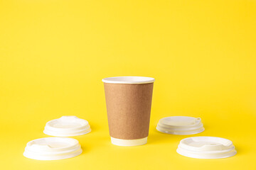 Paper cup and plastic lids on a yellow background isolated.