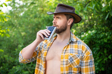 masculine cowboy drink from flask wear hat. photo of masculine cowboy with flask.