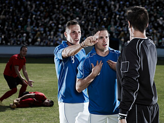 Soccer players arguing with referee on field