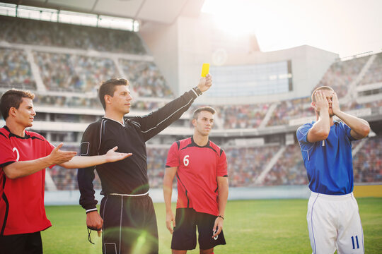 Referee flashing yellow card at soccer player on field