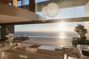 Modern living room overlooking ocean at sunset - obrazy, fototapety, plakaty
