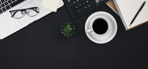 Laptop, glasses, coffee cup and calculator on a black background, top view.