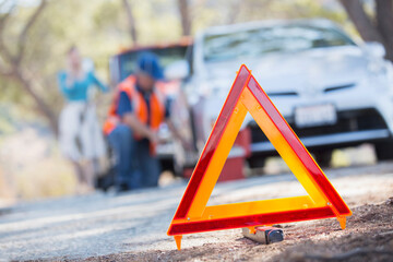 Warning triangle on road with mechanic in background - obrazy, fototapety, plakaty