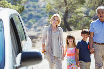 Grandparents and grandchildren holding hands outside car