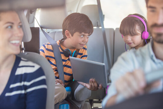 Brother and sister sharing digital tablet in back seat of car