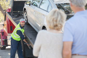 Senior couple watching roadside mechanic prepare to tow car