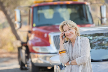 Woman talking on cell phone near tow truck at roadside