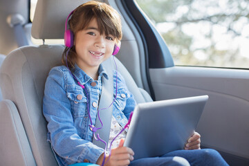 Portrait smiling girl headphones using digital tablet in back seat of car