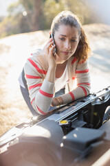 Frustrated woman talking on cell phone and looking at car engine