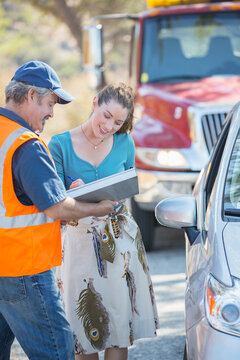 Woman signing paperwork for roadside mechanic