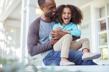 Father tickling daughter on porch