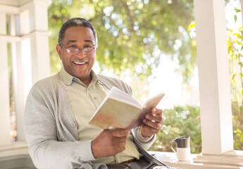 Portrait of smiling senior man reading book on porch