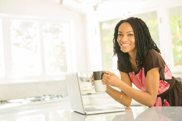 Portrait of smiling woman drinking coffee at laptop in kitchen