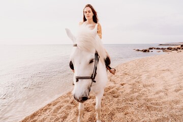 A white horse and a woman in a dress stand on a beach, with the sky and sea creating a picturesque...