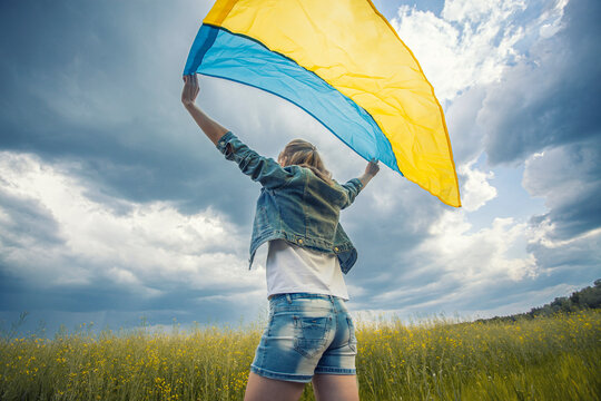 woman with Ukrainian flag in rapeseed field. waving national flag praying for peace. Happy girl celebrating Independence Day.