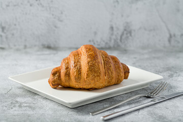Croissant on white porcelain plate on light stone table