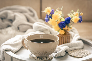 Home composition with a cup of tea and flowers on a blurred background.