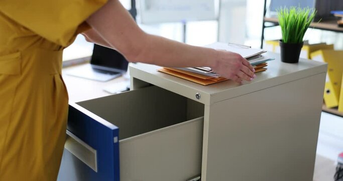 Woman secretary opens drawer and puts documents in office. Storage business documentation