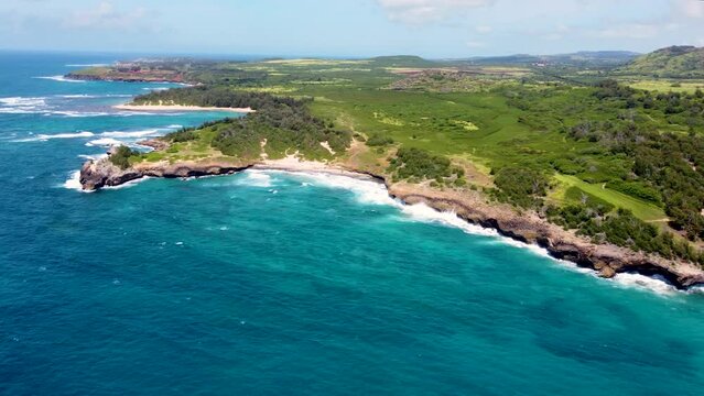 Cinematic aerial shot along the coast of a secluded beach in Koloa Kauai Hawaii USA. Amazing white sand beach, sharp cliffs and tropical lagoon towards beautiful green mountains at Kawaiola Bay