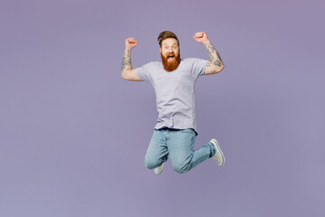 Fototapeta na wymiar Full body young redhead bearded man wear violet t-shirt casual clothes do winner gesture celebrate clenching fists say yes jump high isolated on plain pastel light purple background studio portrait.