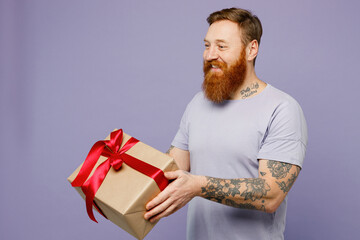 Side view young redhead bearded man he wear violet t-shirt casual clothes hold present box with red...
