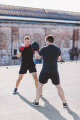 Two men do boxing training on roof of the building in industrial city