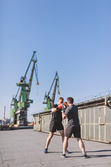 Two men do boxing training on roof of the building in industrial city