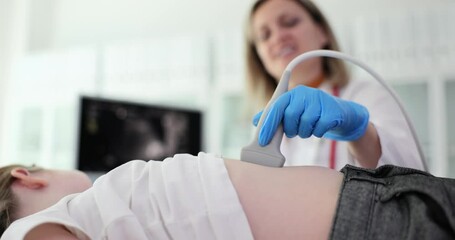 Doctor makes ultrasound of abdominal cavity for girl using scanner. Doctor runs ultrasound probe over patient abdomen while looking at screen
