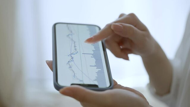 スマートフォンで為替チャートを確認する女性の手元

