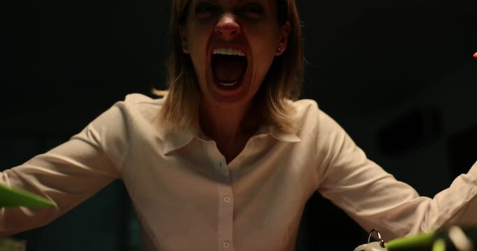 Portrait of angry business woman screaming at office desk late at night during thunderstorm. Emotions of fear of aggression and anger