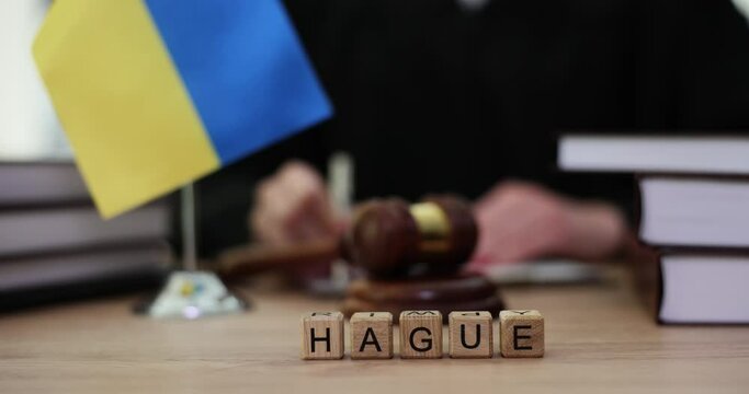 Word hague on cubes and flag of ukraine and judges in courtroom. UN Court in hague ordered Russia to stop hostilities and war on territory of Ukraine