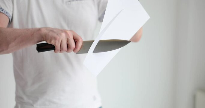 Man demonstrates the sharpness of knife cutting thin sheet of paper. Razor sharp blade