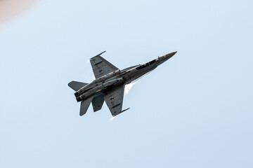 Bottom view of a hornet F-16 jet fighter in Gijon Air show festival doing tricks at subsonic speed in a clear summer blue sky with condensation big steles in its wings