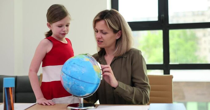 Mother and daughter do geography homework with globe at home. Teacher shows world map on globe to schoolgirl