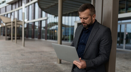 a successful European male journalist with a laptop in his hands works remotely against the backdrop of a business center