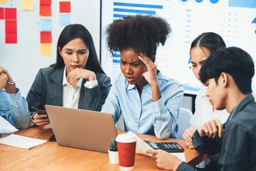 Diverse businesspeople analyzing financial dashboard data on laptop in serious meeting, confused...