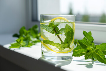 Detox water with mint and lemon on window sill and fresh mint leaves around. Herbal refreshing drink. Homemade antioxidant water.