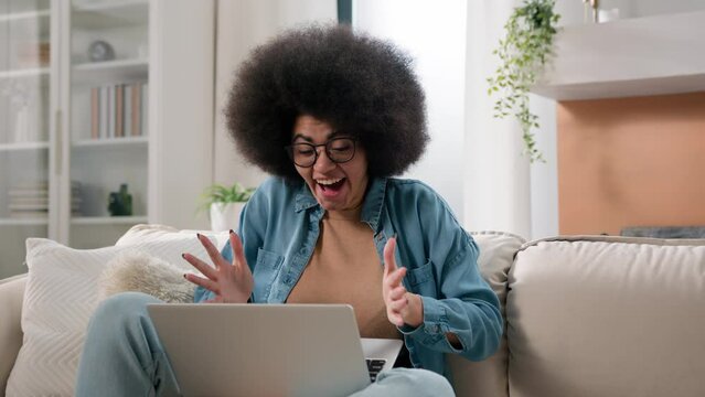 Happy girl winner shock surprise amaze wonder online laptop winning at home couch excited African American successful woman celebrate online success computer victory triumph bet prize on sofa achieve