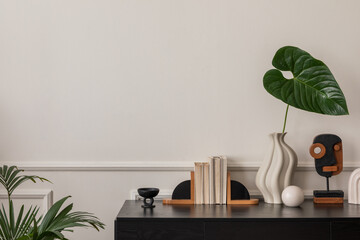 Fototapeta Creative composition of living room interior with copy space, black desk, stylish vase with green leaves, wall with stucco, wooden sculpture, plants and personal accessories. Home decor. Template. obraz