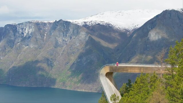 Norwegian blonde on spectacular Stegastein viewpoint with flag; drone reveal