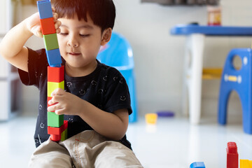 Toddler Asian cute boy playing creative toy blocks at home.  Creative kindergarten kids build a block tower.