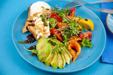 Healthy breakfast. Avocado and salmon, poached egg and toast, salad and vegetables. Microgreens on a plate. Food bowl. Lunch on a blue plate. Sauce and sesame seeds, lemon tomatoes. Top view.