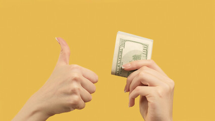 Passive income. Agreed gesture. Woman hands showing dollars and like sign d on orange yellow...