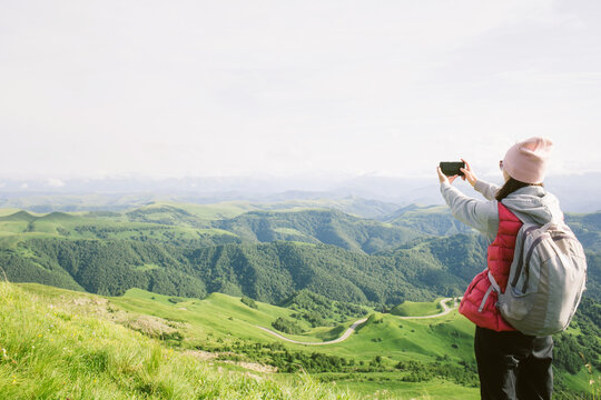 young woman takes pictures on her phone mountain landscape. travel, hiking, journey, outdoor activity