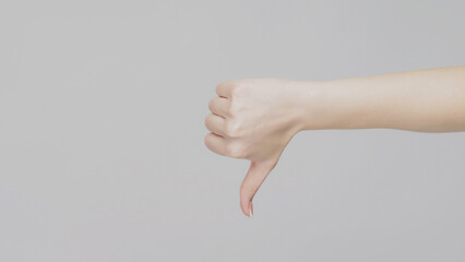 Dislike gestures. Bad idea. Female hand showing thumb down on light gray copy space background.