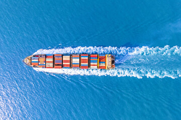 Aerial top view of cargo ship with contrail in the ocean ship carrying container and running.