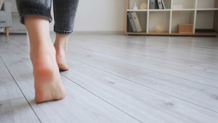 Floor heating. Home barefoot. Unrecognizable woman feet walking on warm laminated wood panels...