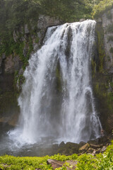Big waterfall in a mountain gorge. Below, a man bathes under a waterfall. Travel on the Kamchatka Peninsula. Beautiful nature of the Russian Far East. Waterfall Spokoyny (Calm), Kamchatka Krai, Russia
