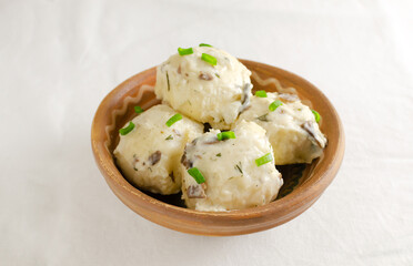 Dumplings stuffed with chicken filling with white mushroom and dill sauce on a clay plate on a white background. Rustic style. Concept Traditional Ukrainian cuisine. Selective focus.