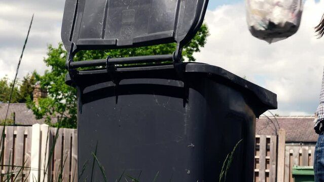 Woman puts garbage in the wheelie bin wide shot